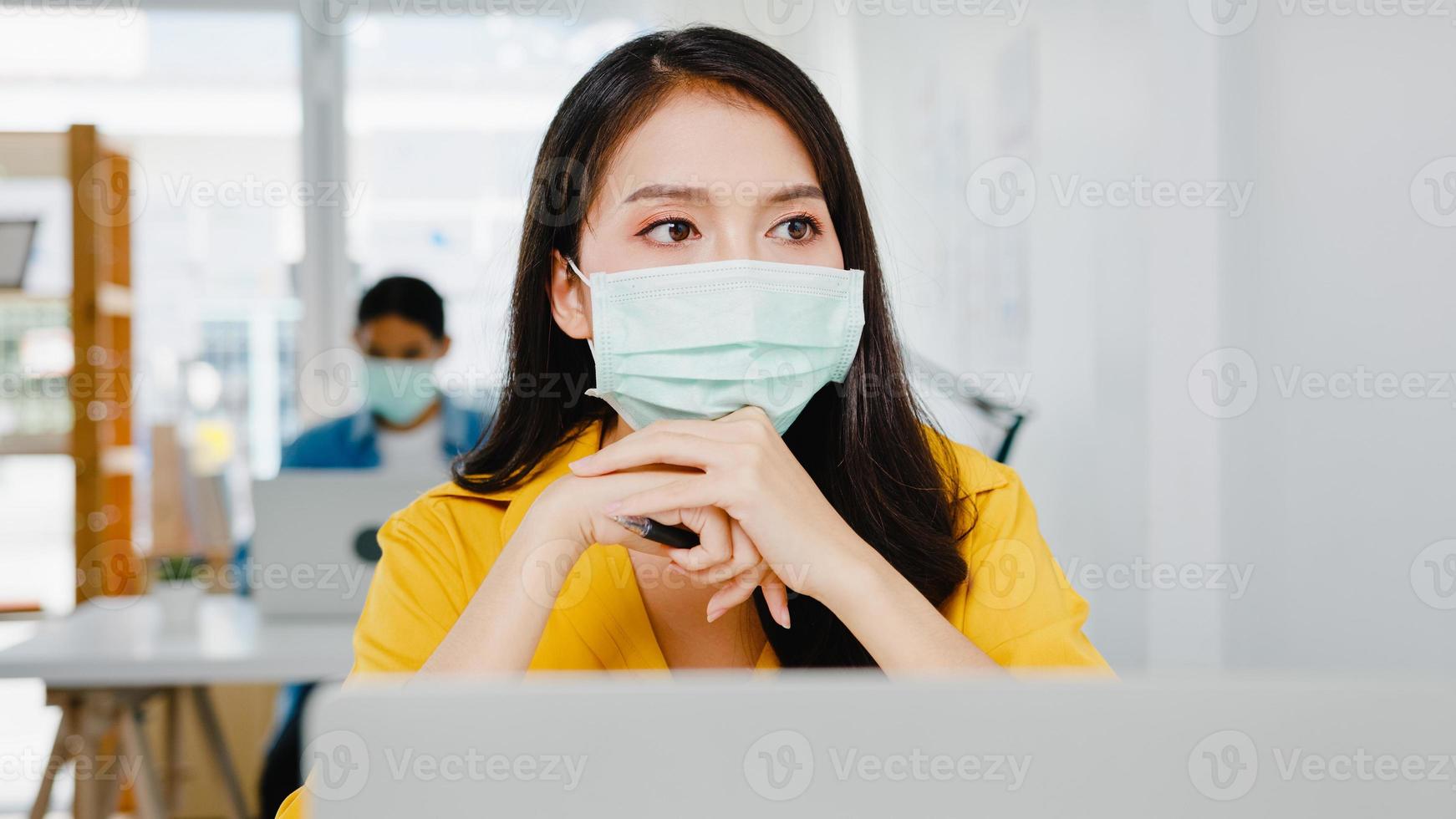 les femmes asiatiques indépendantes portent un masque facial en utilisant un ordinateur portable pour travailler dur dans un nouveau bureau à domicile normal. travailler à partir de la surcharge de la maison, de l'auto-isolement, de la distanciation sociale, de la quarantaine pour la prévention du virus corona. photo