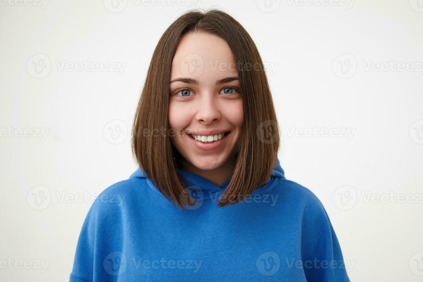 fermer de Jeune heureux charmant court aux cheveux brunette femelle sans pour autant maquillage à la recherche gaiement à caméra avec large sourire tandis que posant plus de blanc Contexte photo