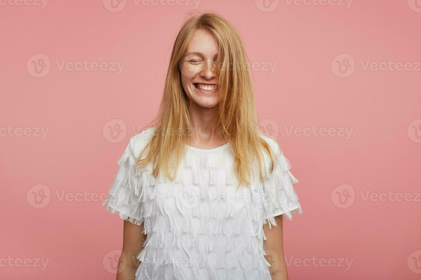 bien à la recherche Jeune de bonne humeur Dame avec rusé cheveux en gardant sa yeux fermé tandis que souriant Heureusement, permanent plus de rose Contexte avec mains bas, habillé dans élégant porter photo