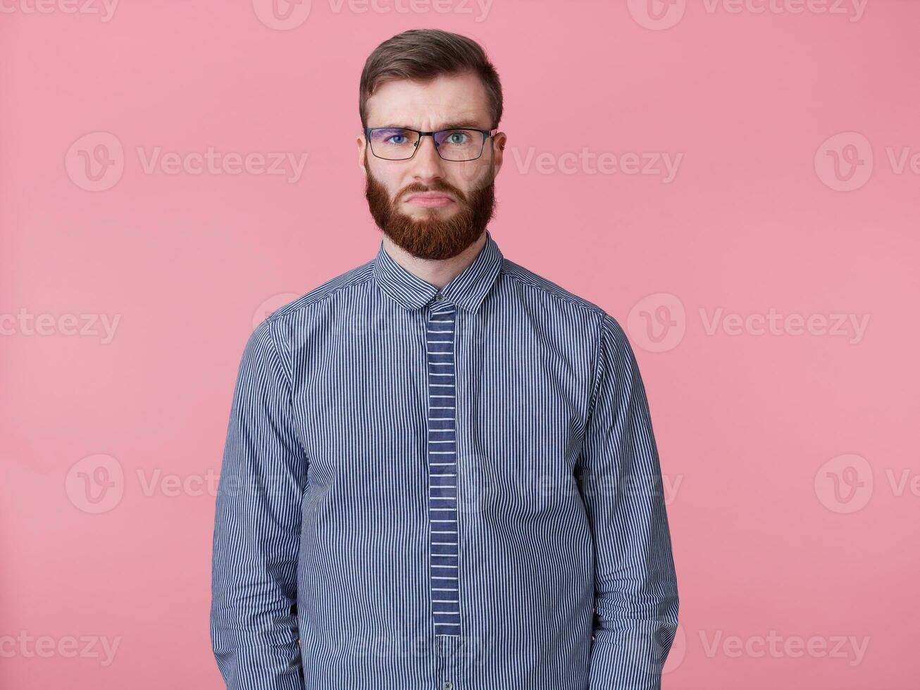 triste Jeune Beau rouge barbu homme avec des lunettes et une rayé chemise, triste cette le fin de le travail la semaine est ne pas bientôt, et il est déjà très fatigué. des stands plus de rose Contexte. photo