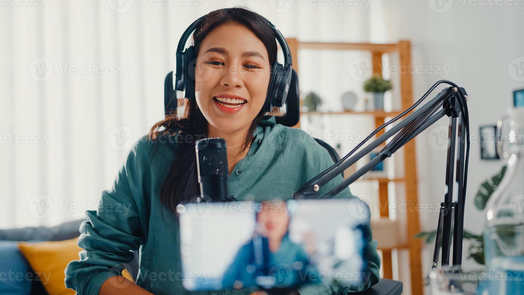 une influenceuse adolescente asiatique utilise un microphone pour porter un contenu d'enregistrement de casque avec un téléphone intelligent pour le public en ligne, écouter à la maison. une étudiante podcasteuse crée un podcast audio depuis son home studio. photo