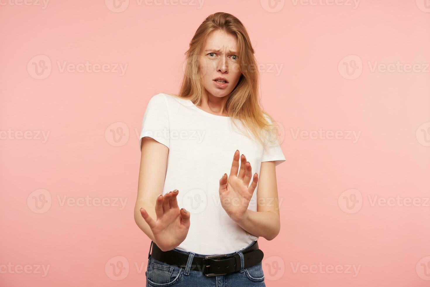 studio photo de Jeune confus roux femme avec décontractée coiffure élevage paumes dans protecteur geste tandis que à la recherche avec peur à caméra, isolé plus de rose Contexte