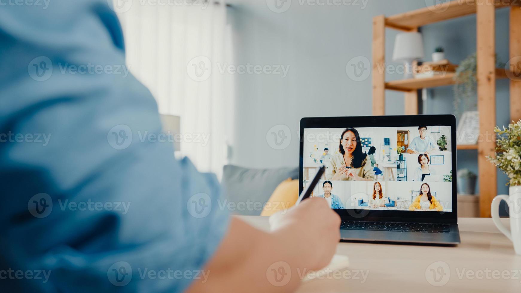un jeune homme d'affaires asiatique utilisant un ordinateur portable parle à ses collègues du plan lors d'une réunion par appel vidéo pendant qu'il travaille à domicile dans le salon. auto-isolement, distanciation sociale, quarantaine pour la prévention du virus corona. photo