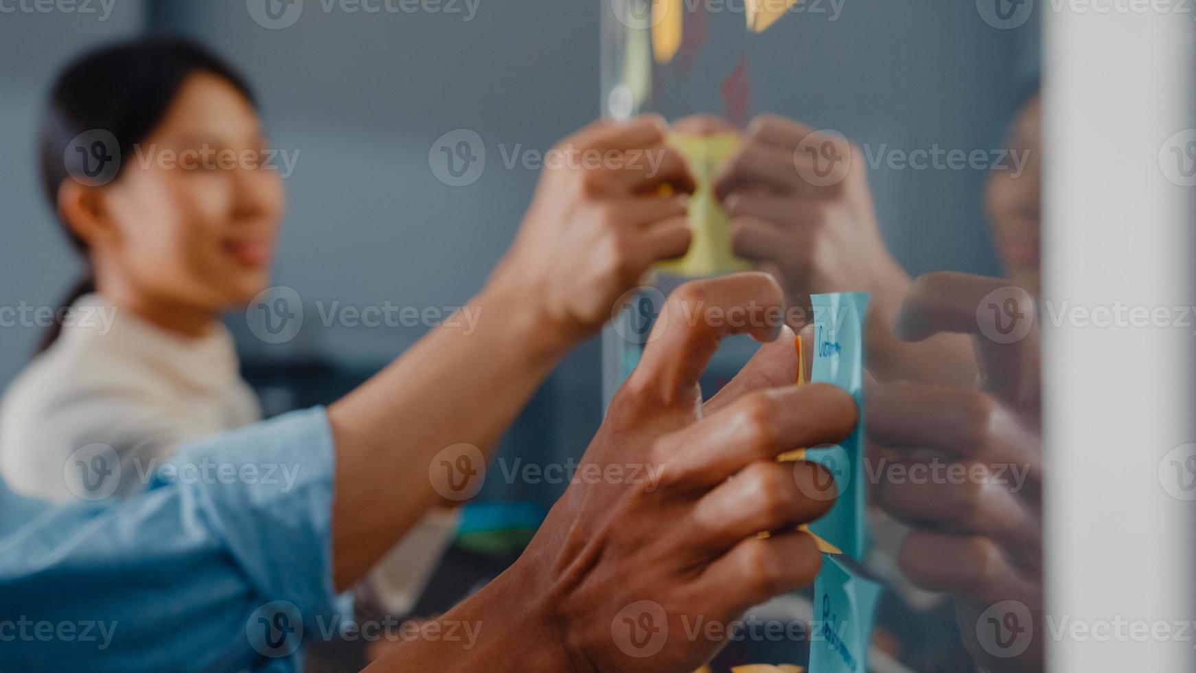 les hommes d'affaires d'asie se tiennent derrière un mur de verre transparent, écoutent le directeur pointant les travaux d'avancement et la réunion de remue-méninges et le travailleur publie une note collante sur le mur au bureau. inspiration d'affaires, partager des idées. photo