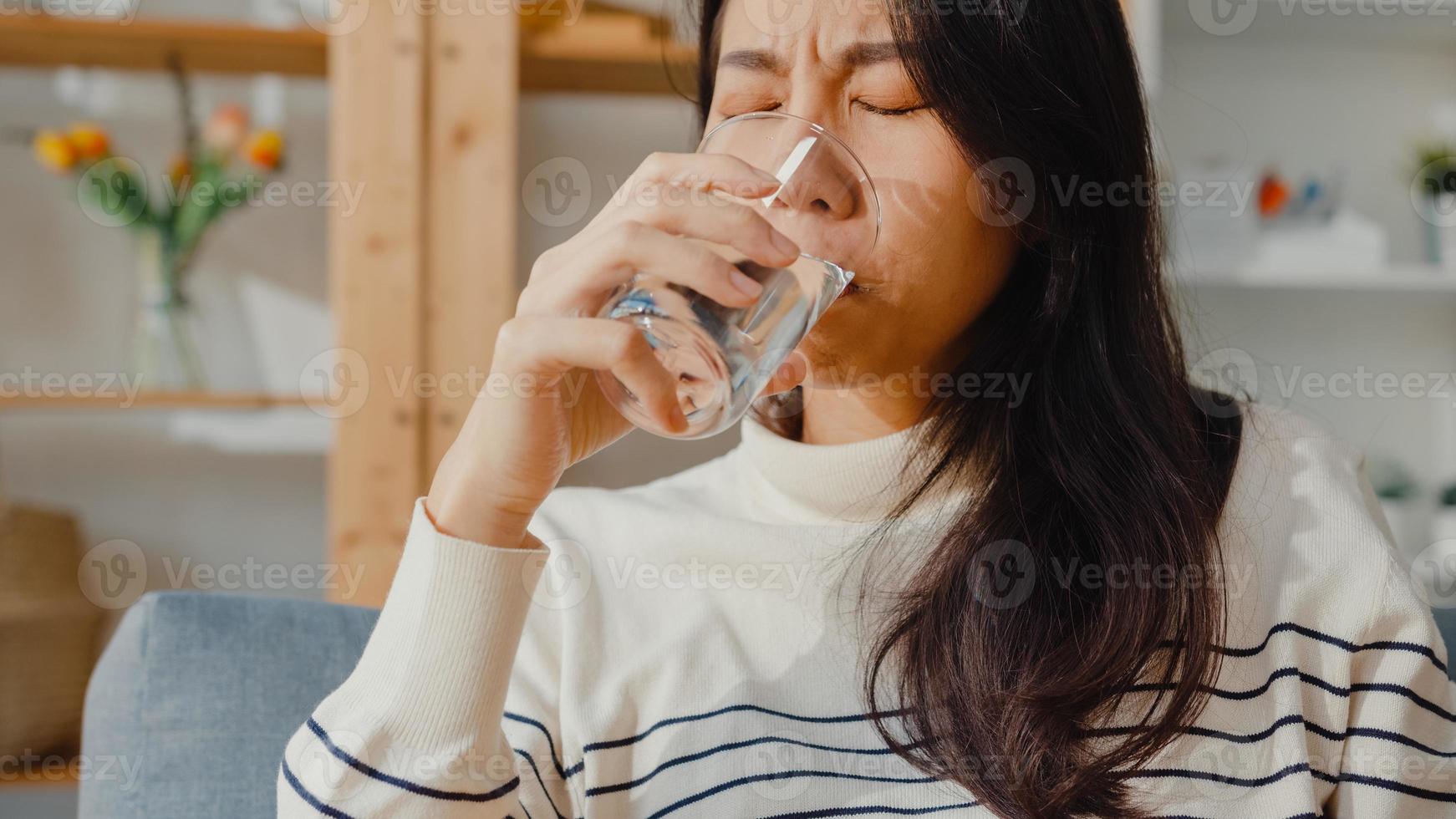 jeune femme asiatique malade tenant une pilule verre d'eau prendre des médicaments s'asseoir sur un canapé à la maison. fille prenant des médicaments après ordre du médecin, quarantaine à la maison, concept de quarantaine de distanciation sociale du coronavirus. photo