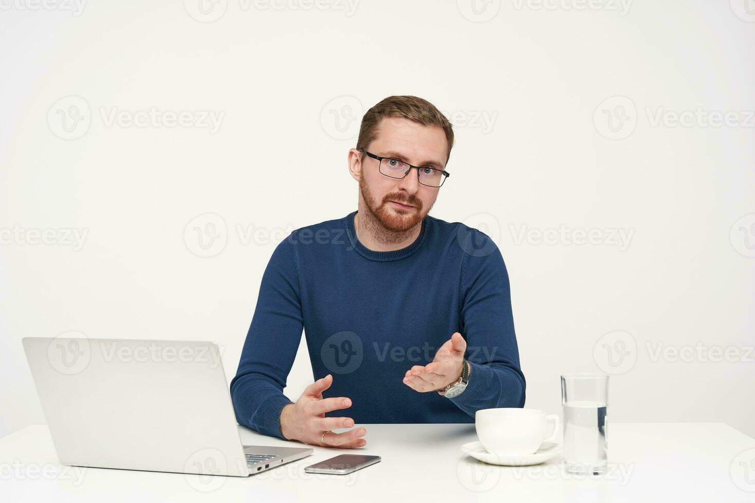 perplexe Jeune jolie barbu gars dans lunettes à la recherche confusément à caméra et élevage avec perplexité palmier, isolé plus de blanc Contexte dans bleu arrêtez-vous photo