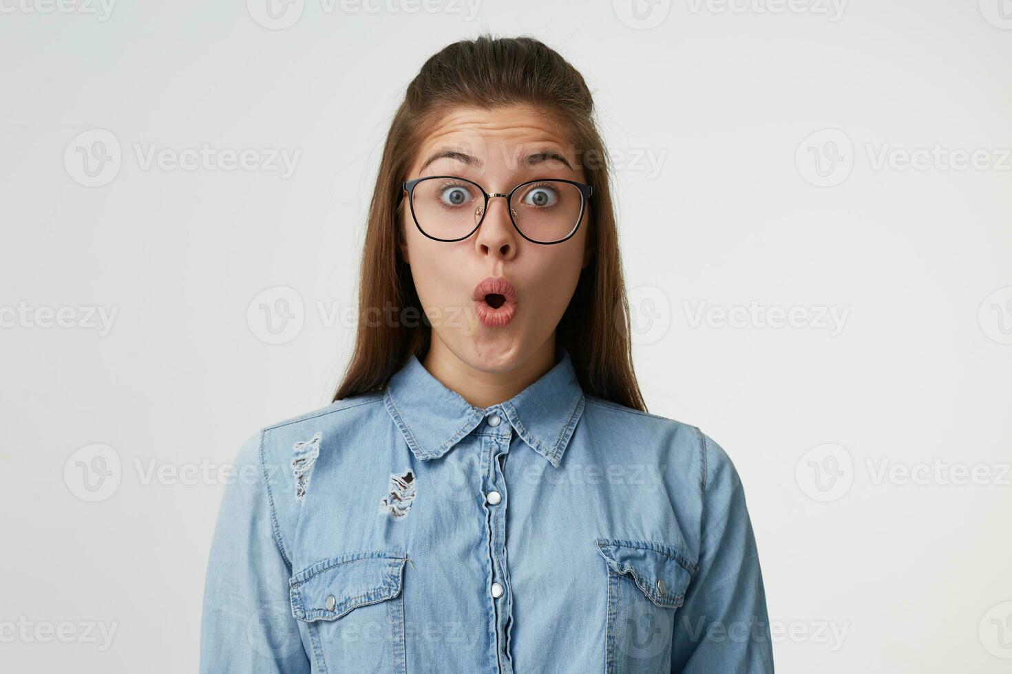 proche en haut visage de une Jeune fille avec longue cheveux dans des lunettes regards surpris, étonné, choqué. femme a trouvé en dehors incroyable nouvelles, été témoin inoubliable un événement sur une blanc Contexte photo