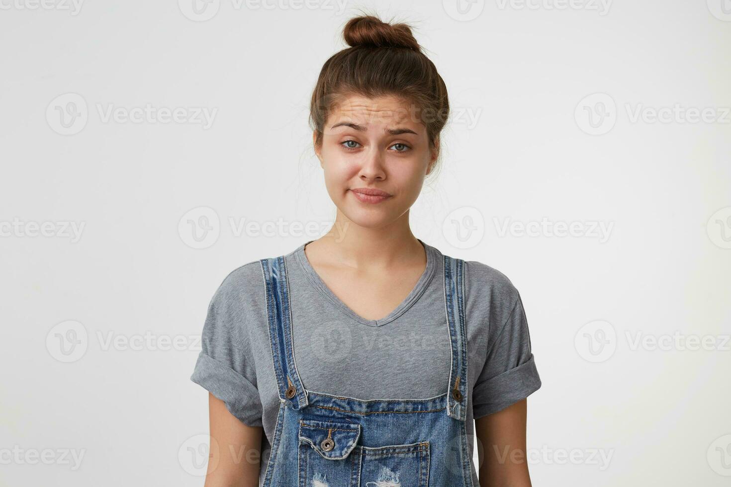 proche en haut visage de une Jeune fille avec cheveux recueillies dans une chignon porte denim global, Regardez sceptique avec incrédulité avec mépris, une coin de lèvres pincé, les sourcils fronça les sourcils photo