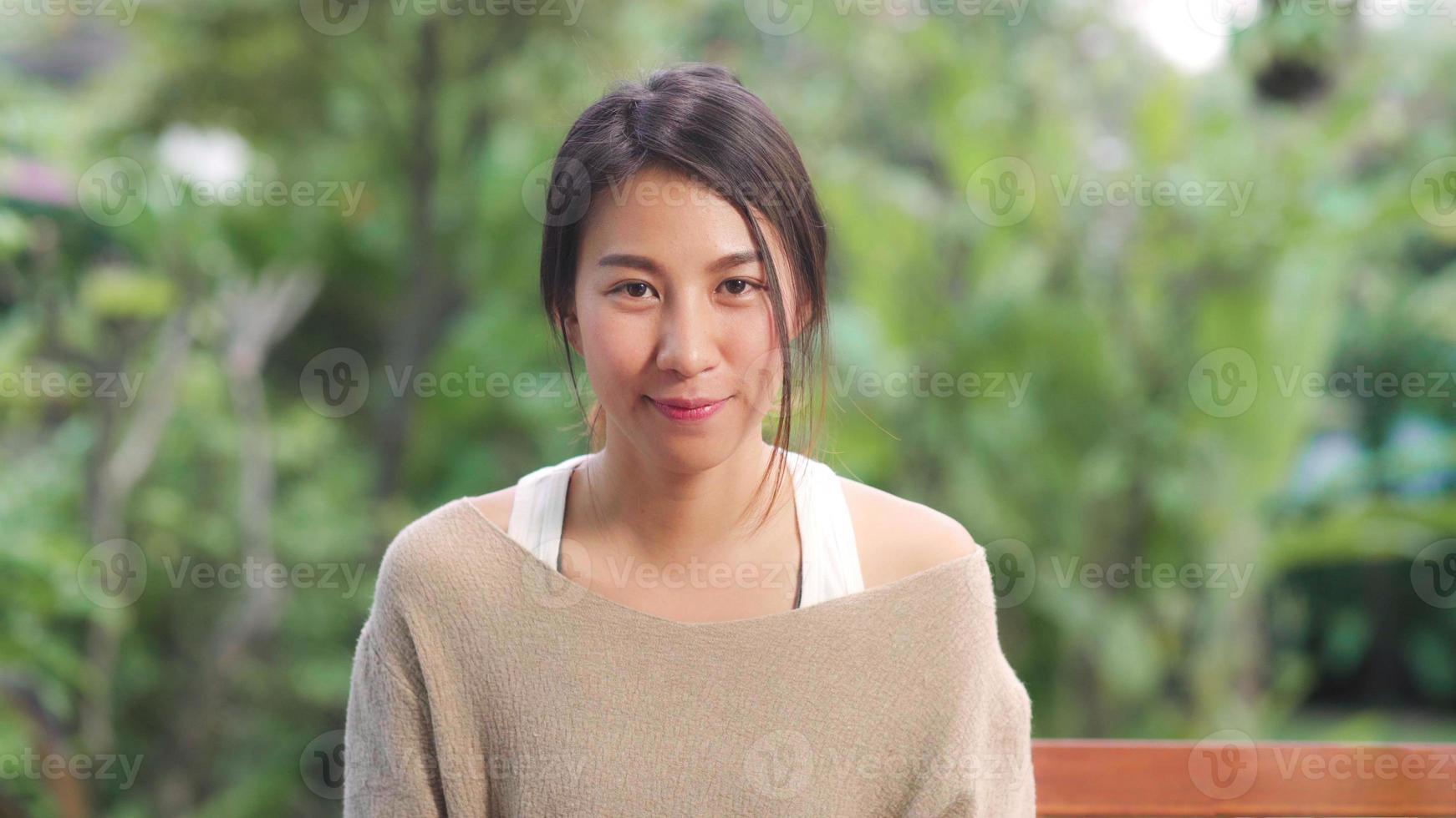 femme asiatique se sentant heureuse en souriant et en regardant la caméra tout en se relaxant sur la table dans le jardin à la maison le matin. les femmes de style de vie se détendent à la maison concept. photo