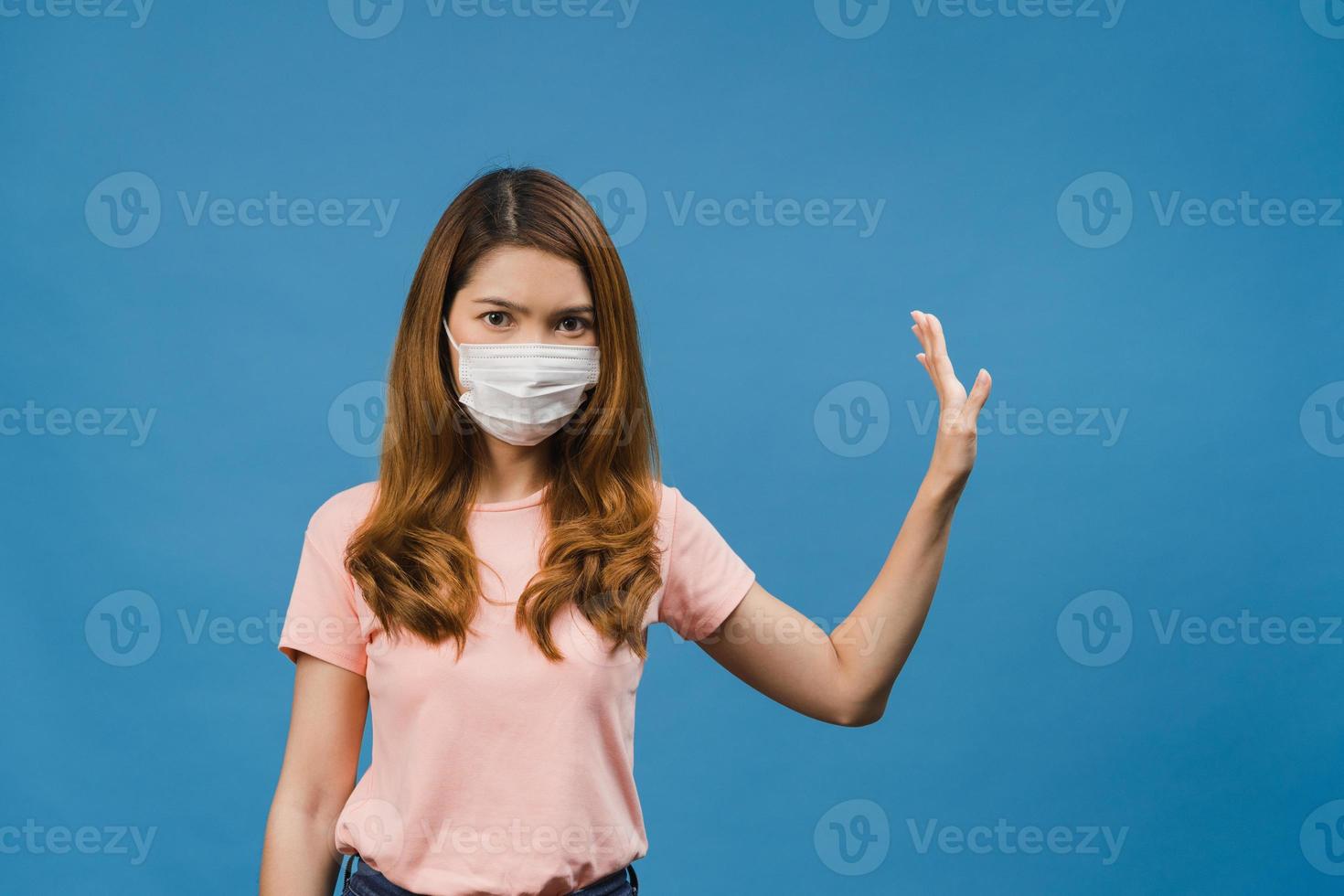 une jeune femme asiatique porte un masque médical en arrêtant de chanter avec la paume de la main avec une expression négative et en regardant la caméra isolée sur fond bleu. distanciation sociale, quarantaine pour le virus corona. photo