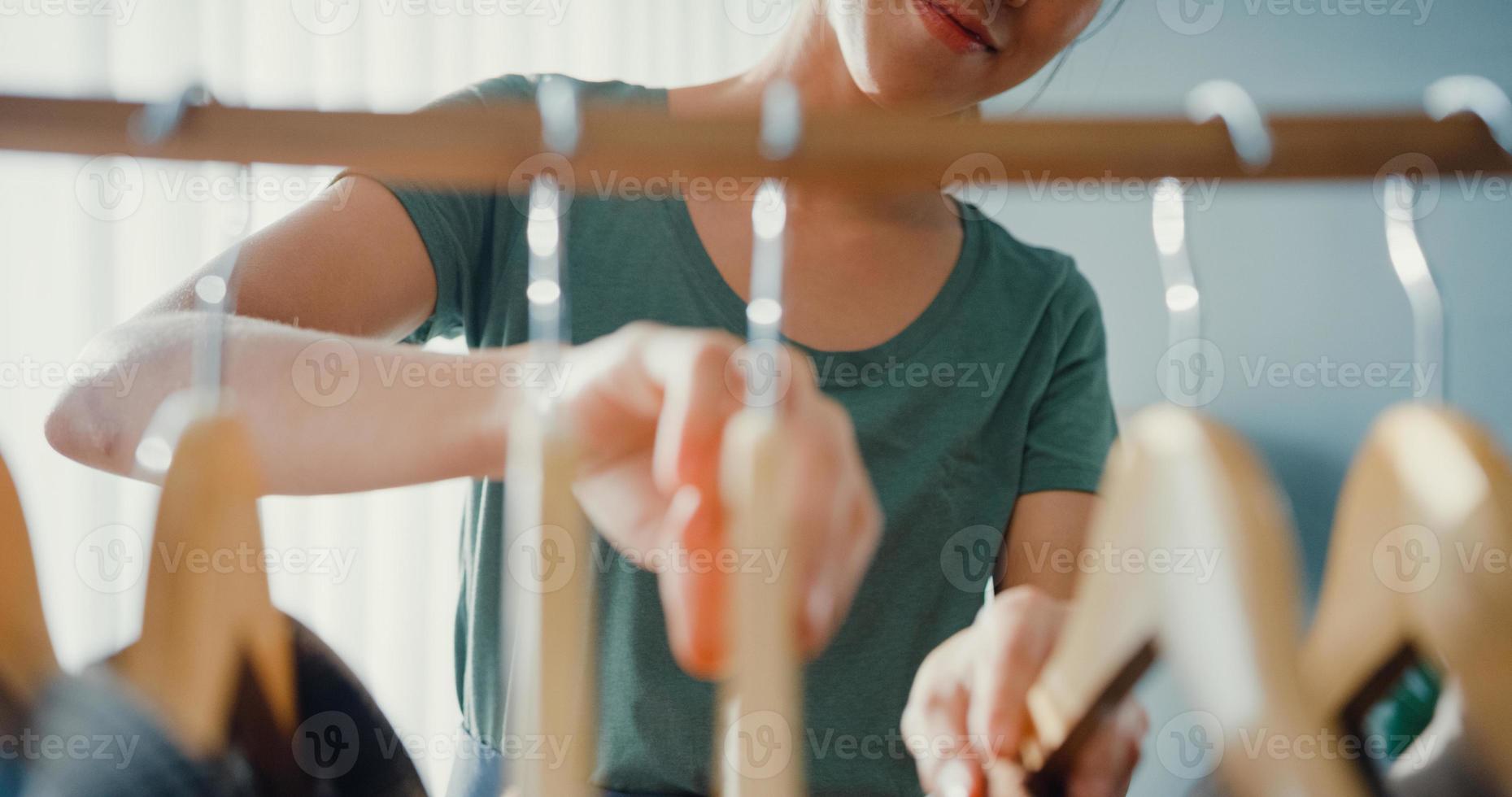 belle jeune femme asiatique séduisante choisissant ses vêtements de mode dans le salon du placard à la maison ou au magasin. fille pense quoi porter chemise décontractée. garde-robe à la maison ou vestiaire de magasin de vêtements. photo