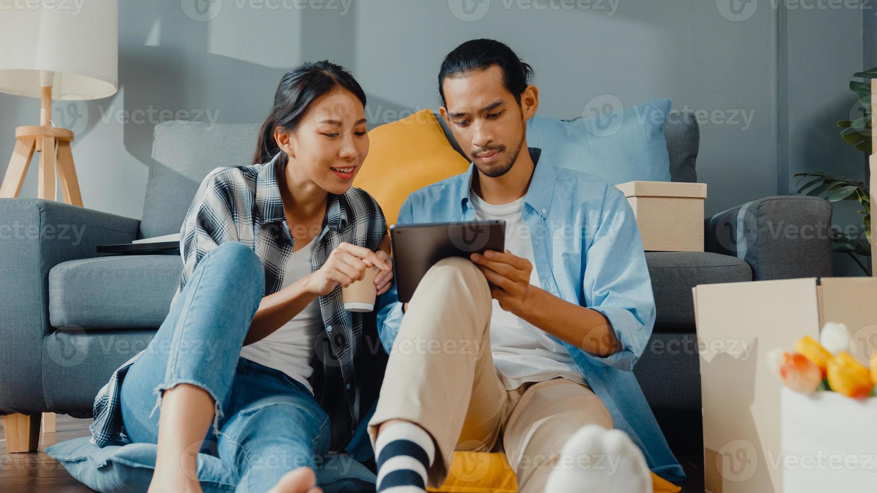 Heureux jeune couple asiatique séduisant homme et femme utiliser une tablette pour acheter des meubles en ligne décorer une maison avec un emballage en carton déménager dans une nouvelle maison. concept en ligne de jeune acheteur de déménagement asiatique marié. photo