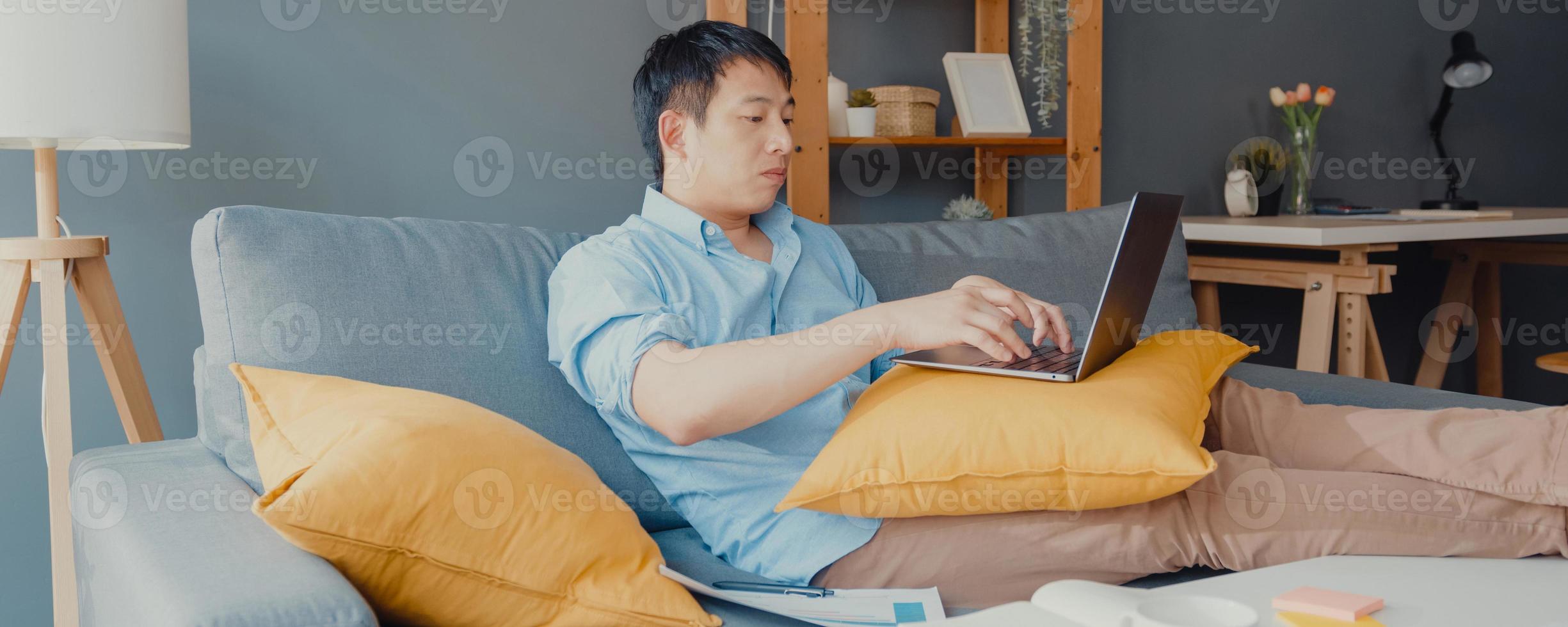 vêtements décontractés pour hommes asiatiques indépendants utilisant un ordinateur portable apprenant en ligne dans le salon de la maison. travail à domicile, travail à distance, enseignement à distance, distance sociale, fond de bannière panoramique avec espace de copie. photo