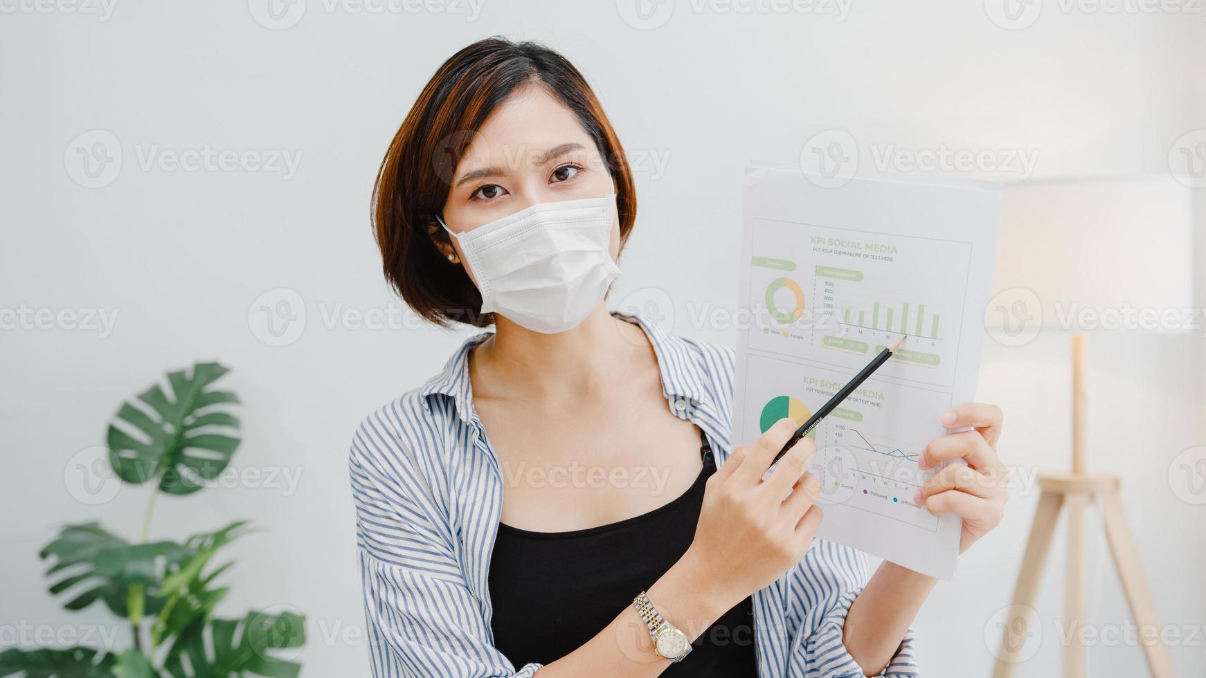 une femme d'affaires asiatique porte un masque facial pour la distanciation sociale en situation de prévention des virus en regardant la présentation de la caméra à un collègue sur le plan du travail d'appel vidéo au bureau. mode de vie après le virus corona. photo