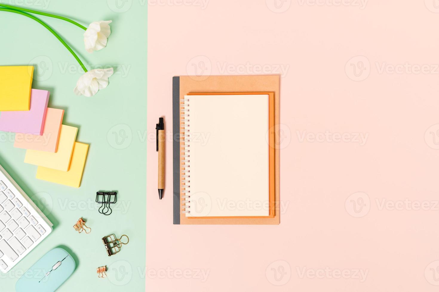 photo créative à plat du bureau de l'espace de travail. bureau vue de dessus avec clavier, souris et cahier noir maquette ouverte sur fond de couleur rose vert pastel. vue de dessus maquette avec copie espace photographie.