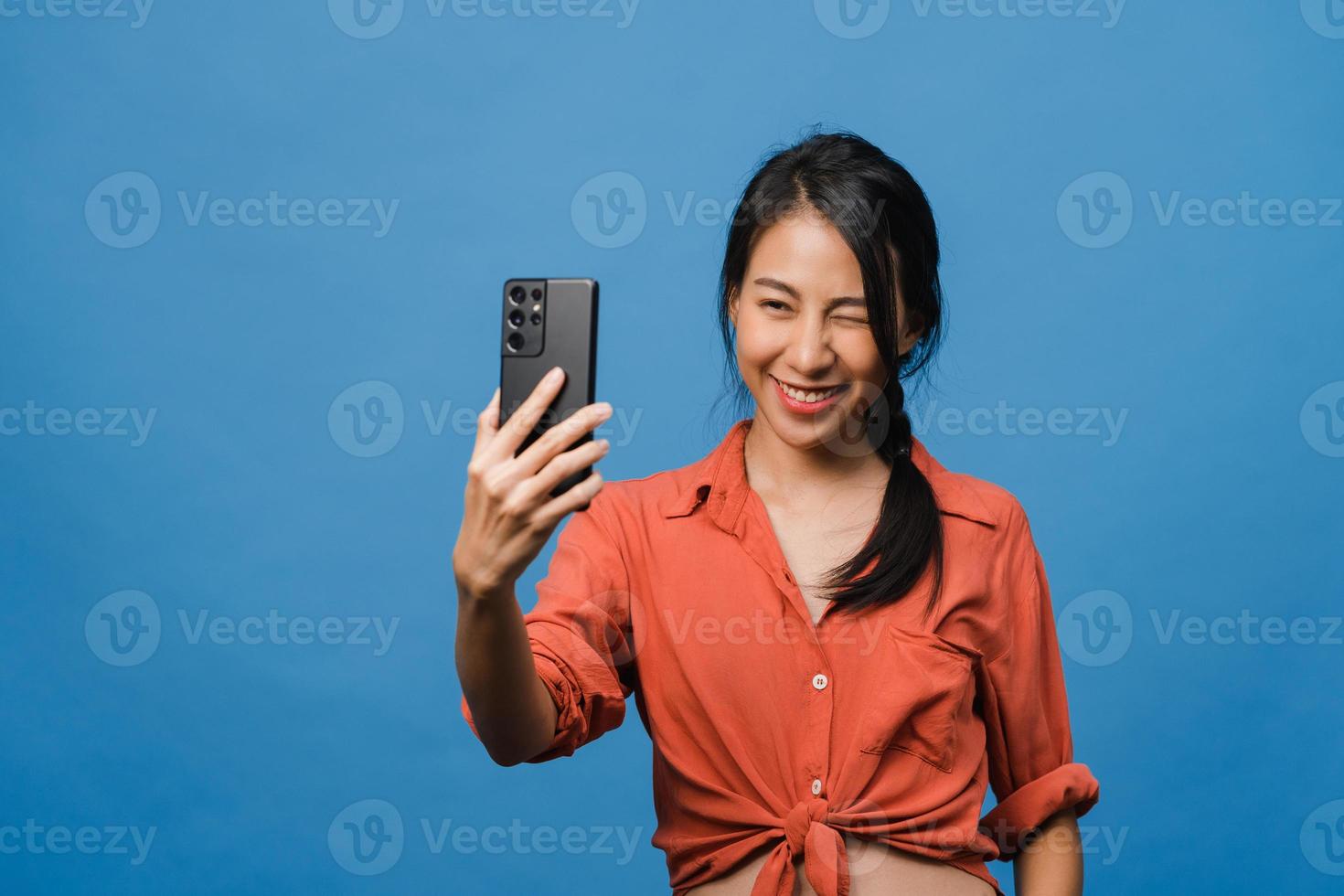souriante adorable femme asiatique faisant une photo de selfie sur un téléphone intelligent avec une expression positive dans des vêtements décontractés et debout isolée sur fond bleu. heureuse adorable femme heureuse se réjouit du succès.