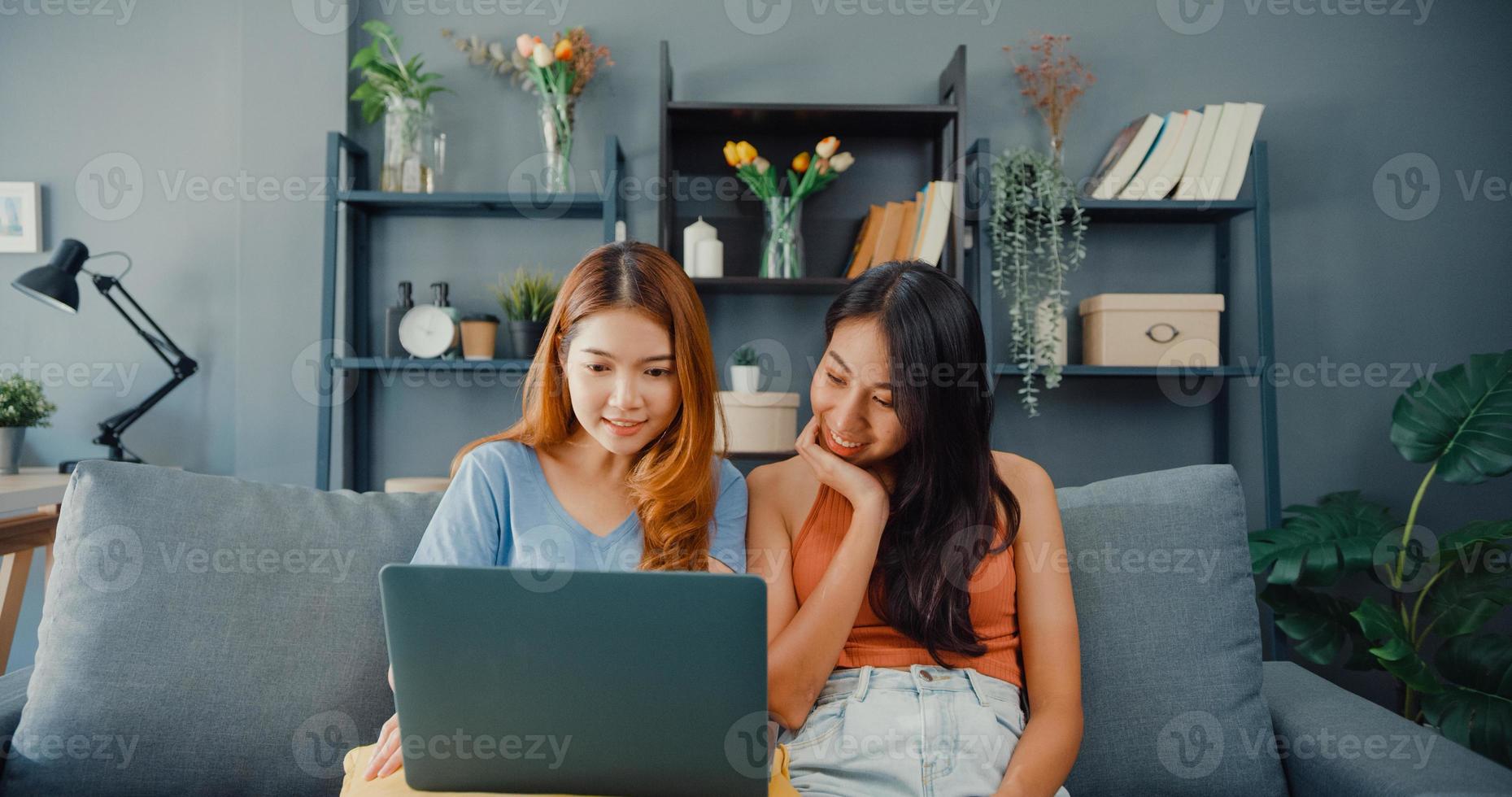 site de deux femmes lesbiennes asiatiques sur un canapé ensemble en regardant un écran d'ordinateur portable dans le salon à la maison ensemble. couple heureux colocataires apprécient la navigation sur le Web, les achats en ligne, le concept de femme de style de vie à la maison. photo