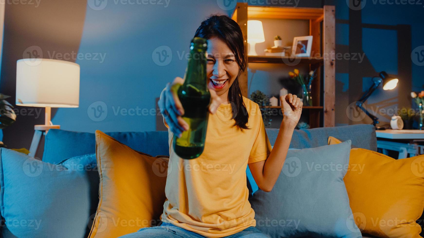 heureuse jeune femme asiatique regardant la caméra profiter d'une soirée en ligne avec des amis, boire de la bière par appel vidéo en ligne dans le salon à la maison, rester à la maison en quarantaine, concept de distanciation sociale. photo