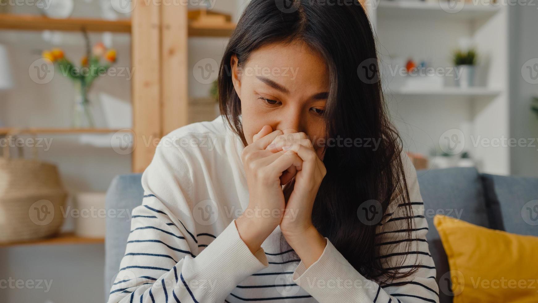 une dame asiatique réfléchie s'assoit embrassant les genoux sur un canapé dans le salon de la maison regarde à l'extérieur avec une sensation de solitude, un adolescent triste et déprimé passe du temps seul à la maison, à distance sociale, quarantaine de coronavirus. photo