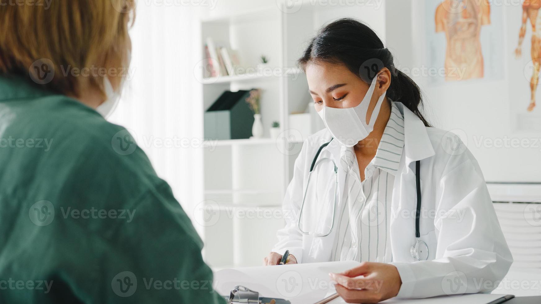 une jeune femme médecin asiatique porte un masque de protection à l'aide d'un presse-papiers donne d'excellentes nouvelles discute des résultats ou des symptômes avec une patiente au bureau de l'hôpital. mode de vie nouveau normal après le virus corona. photo