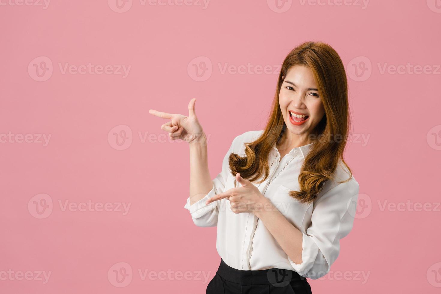 portrait d'une jeune femme asiatique souriante avec une expression joyeuse, montre quelque chose d'étonnant dans un espace vide dans des vêtements décontractés et regardant la caméra isolée sur fond rose. concept d'expression faciale. photo