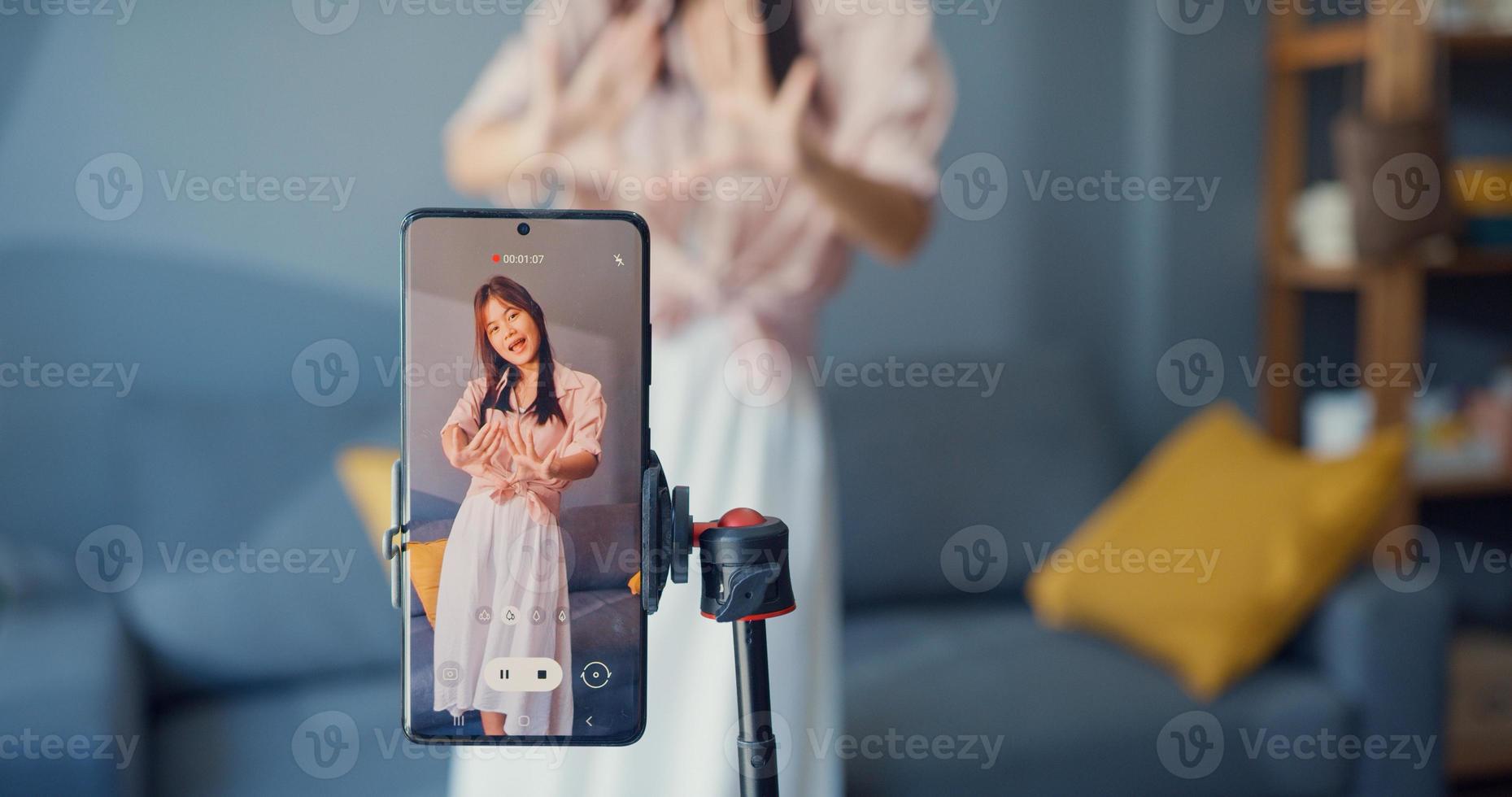 heureuse jeune blogueuse asiatique devant la caméra du téléphone enregistrez une vidéo avec du contenu de danse dans le salon à la maison. concept de pandémie de coronavirus à distance sociale. concept de liberté et de mode de vie actif photo