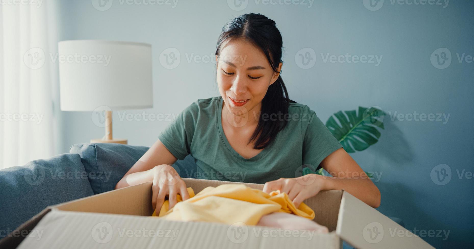 happy asia lady ouvrir le paquet de boîte en carton excitant et profiter d'essayer et d'assortir avec la qualité du produit en tissu de mode du marché en ligne dans le salon à la maison. concept d'achat et de livraison en ligne. photo