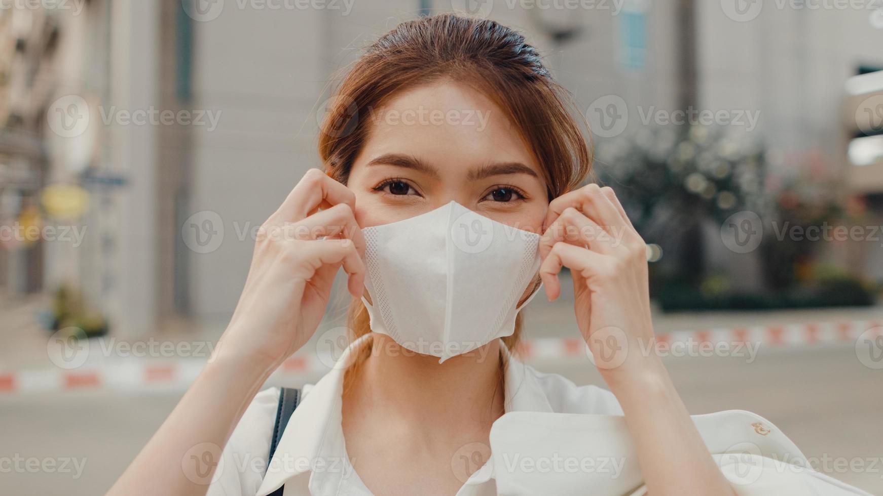 Une jeune femme d'affaires asiatique réussie dans des vêtements de bureau de mode porte un masque médical souriant et regardant la caméra tout en étant heureuse seule à l'extérieur dans une ville urbaine moderne. concept d'entreprise en déplacement. photo