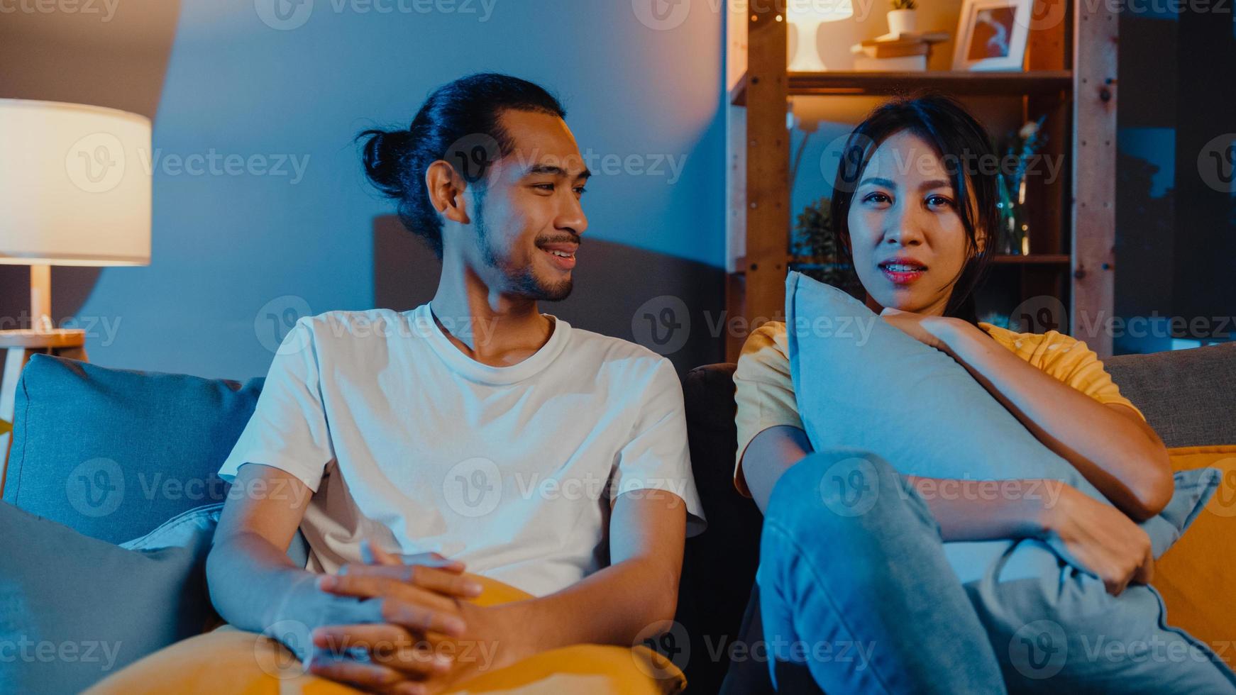 couple d'asie romantique homme et femme sourire et rire s'allonger sur le canapé dans le salon la nuit regarder un film de comédie à la télévision ensemble à la maison. couple marié mode de vie familial, concept de séjour à la maison. photo