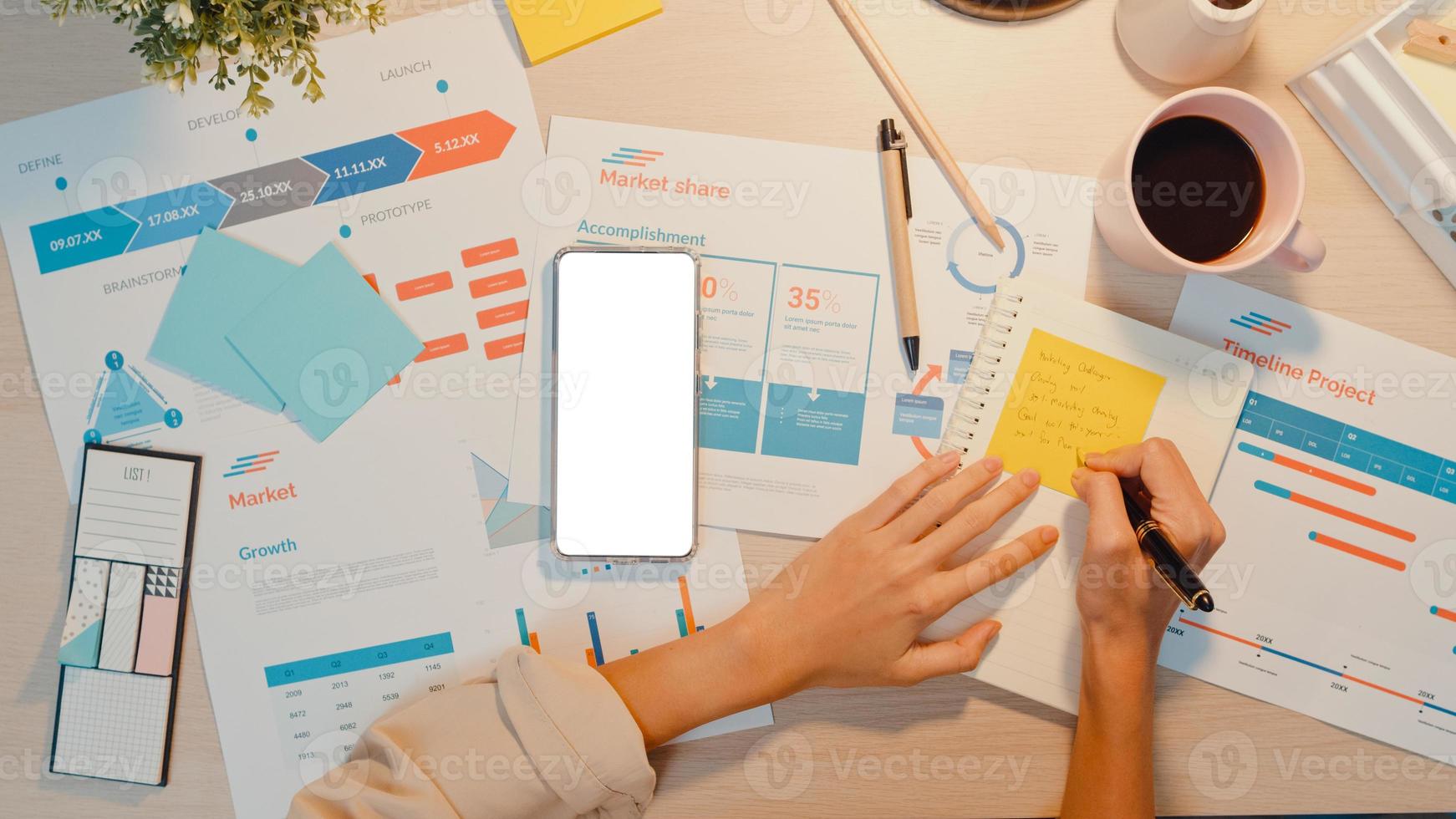 vue de dessus d'une jeune femme d'asie indépendante utiliser un téléphone avec un écran blanc vierge pour afficher du texte publicitaire et écrire une feuille de calcul financière graphique de compte plan de marché la nuit au bureau. clé chroma. photo