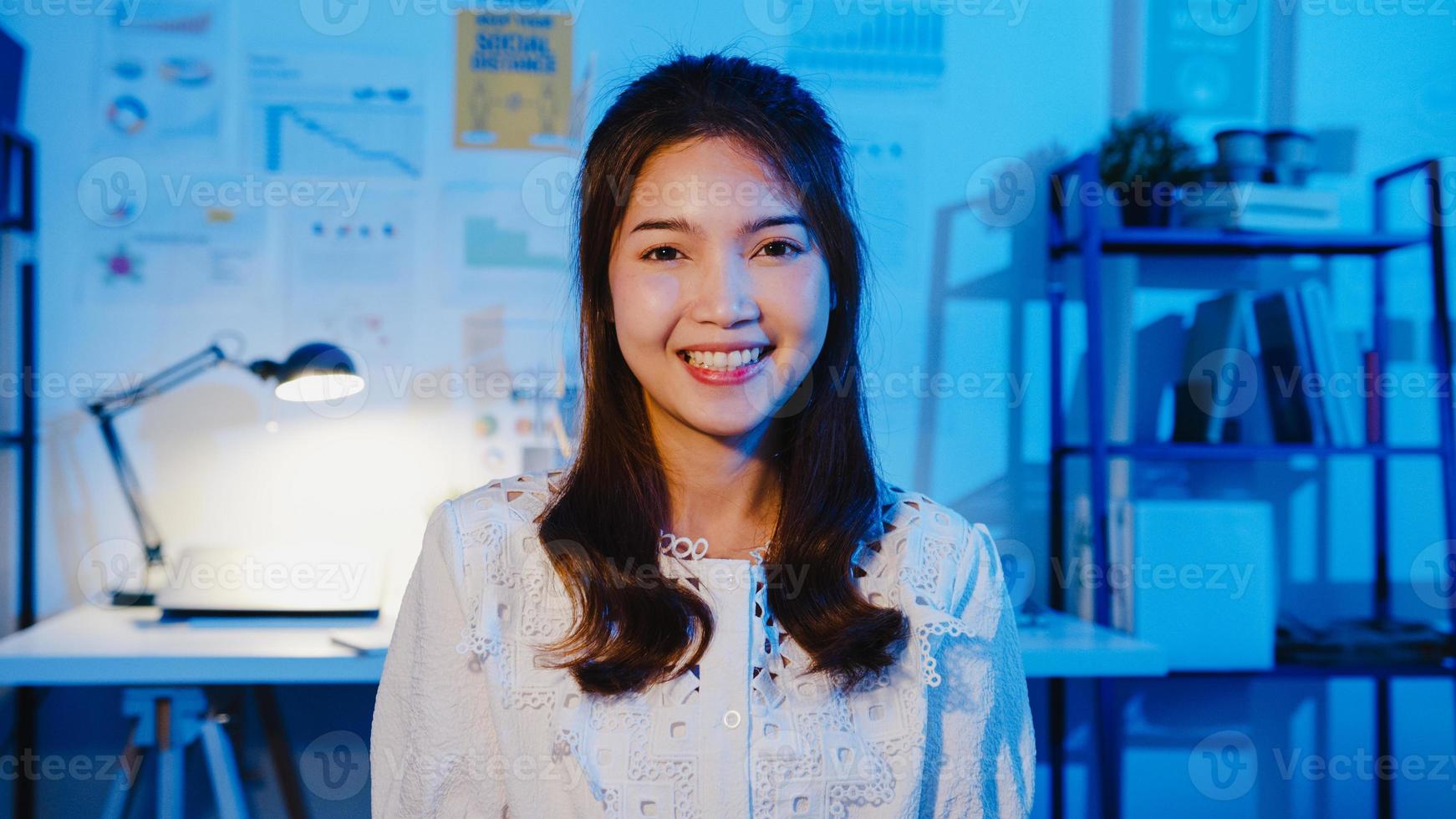 portrait de belle femme d'affaires exécutive vêtements décontractés intelligents regardant la caméra et souriant, heureux dans la nuit de travail de bureau moderne. une jeune femme asiatique parle à un collègue lors d'une réunion par appel vidéo à la maison. photo