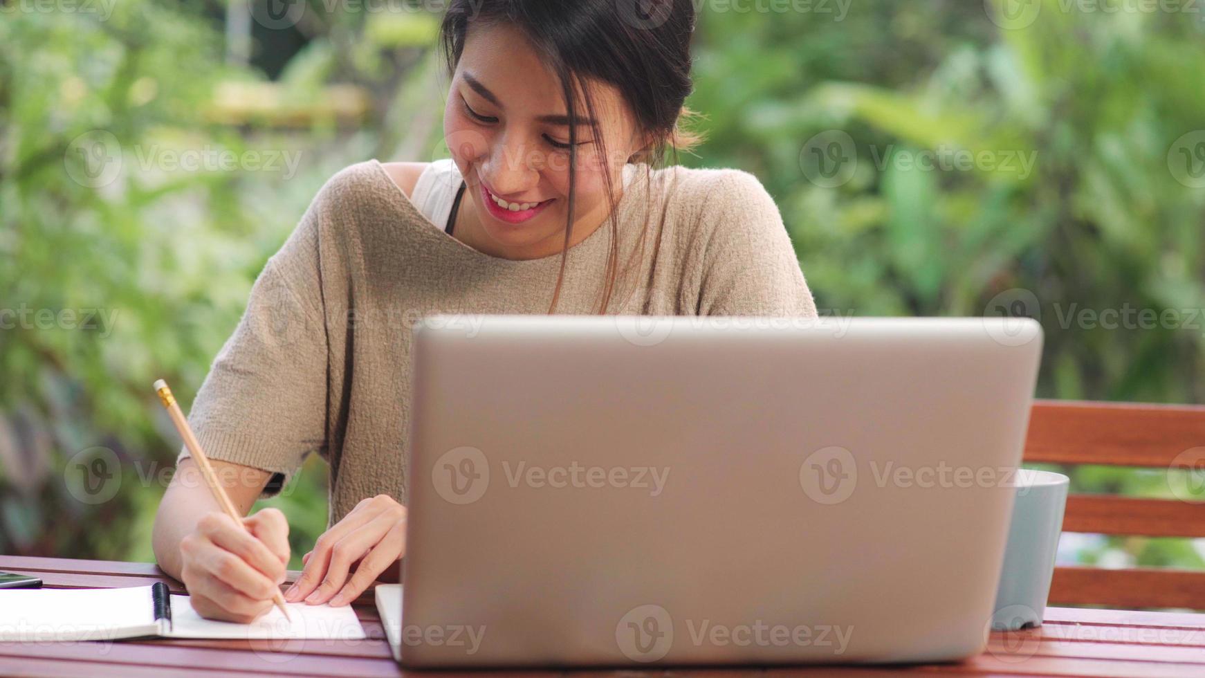 femme asiatique indépendante travaillant à la maison, femme d'affaires travaillant sur ordinateur portable assise sur une table dans le jardin le matin. femmes de style de vie travaillant à la maison concept. photo