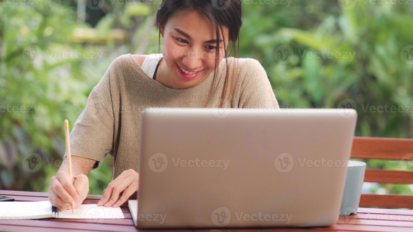 femme asiatique indépendante travaillant à la maison, femme d'affaires travaillant sur ordinateur portable assise sur une table dans le jardin le matin. femmes de style de vie travaillant à la maison concept. photo