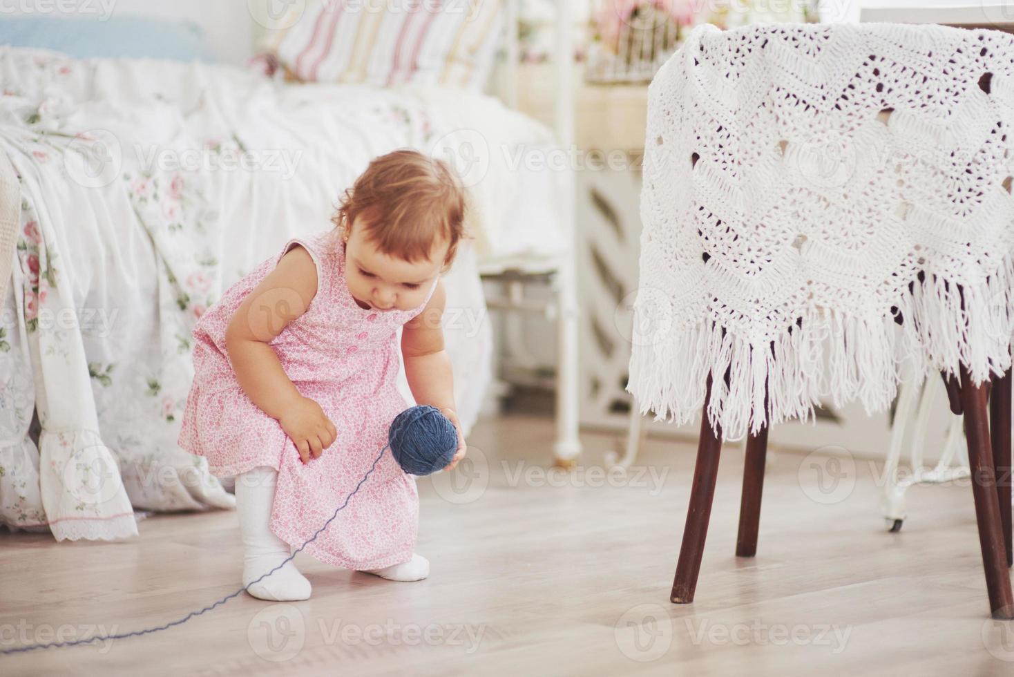 notion d'enfance. petite fille en robe mignonne joue avec du fil coloré. chambre d'enfant vintage blanche photo