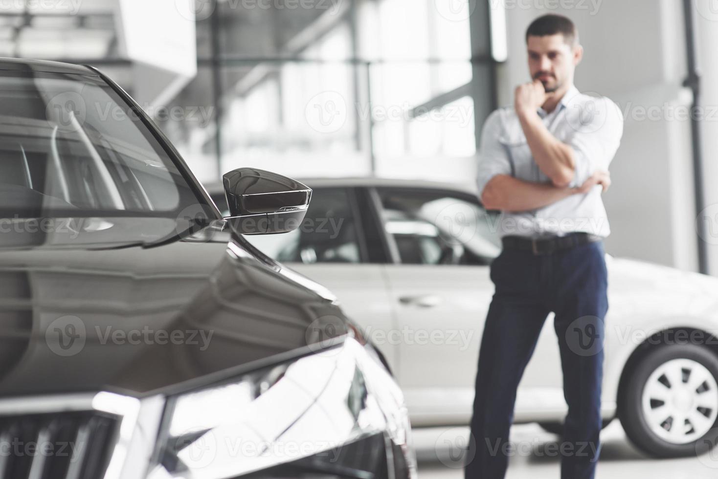 consultant beau jeune homme au salon de l'automobile debout près de la voiture. photo