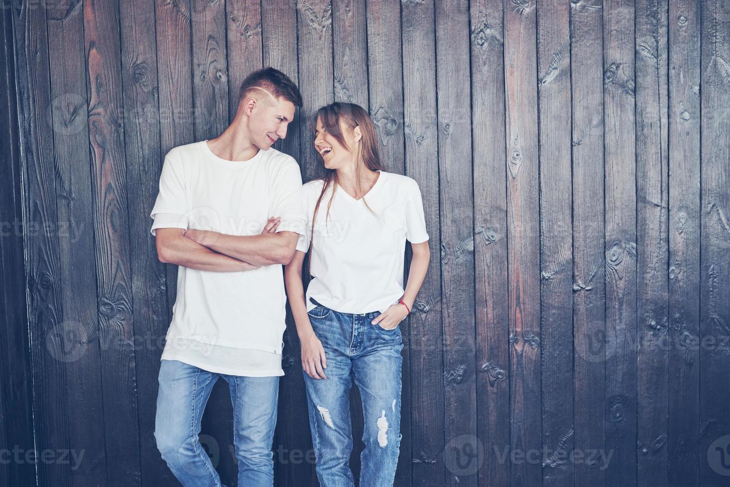 jeune couple, gars et fille ensemble sur un fond de mur en bois. ils sont heureux ensemble et habillés de la même manière. toujours dans la tendance photo