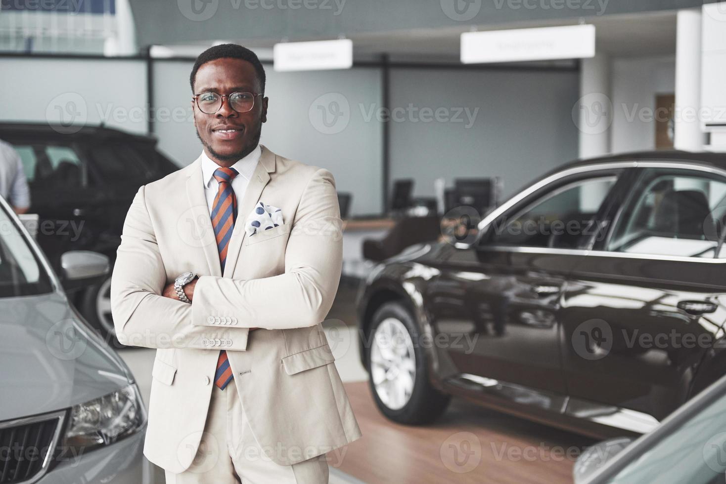jeune homme d'affaires noir sur fond de salon automobile. concept de vente et de location de voiture photo