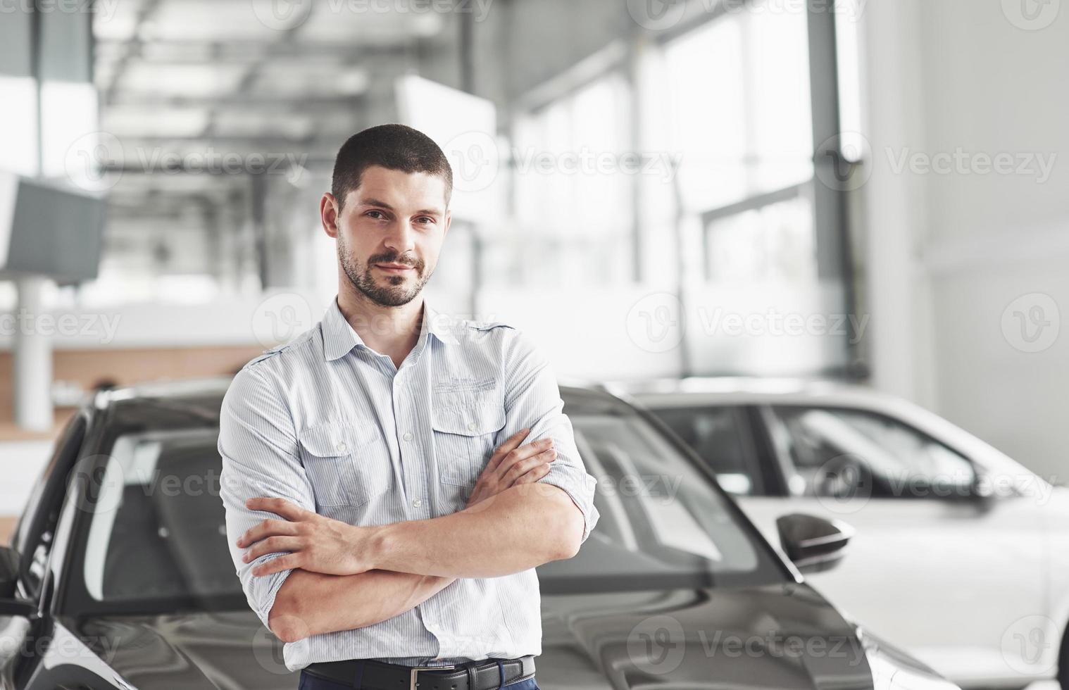 consultant beau jeune homme au salon de l'automobile debout près de la voiture. photo