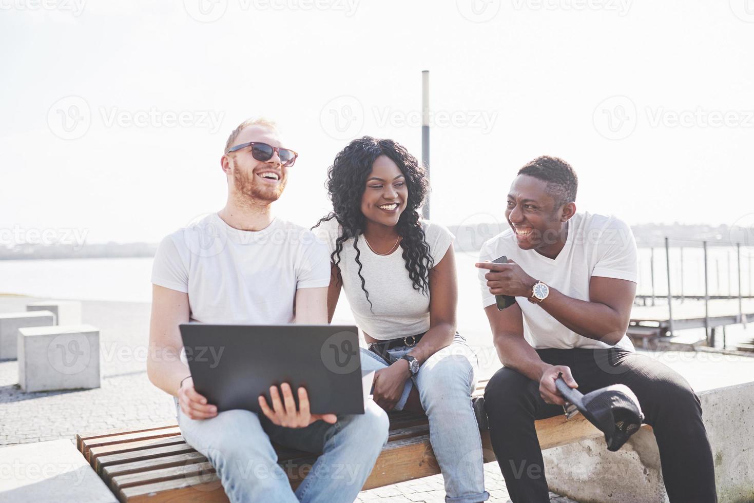beaux amis multiethniques utilisant un ordinateur portable dans la rue. concept de mode de vie des jeunes photo