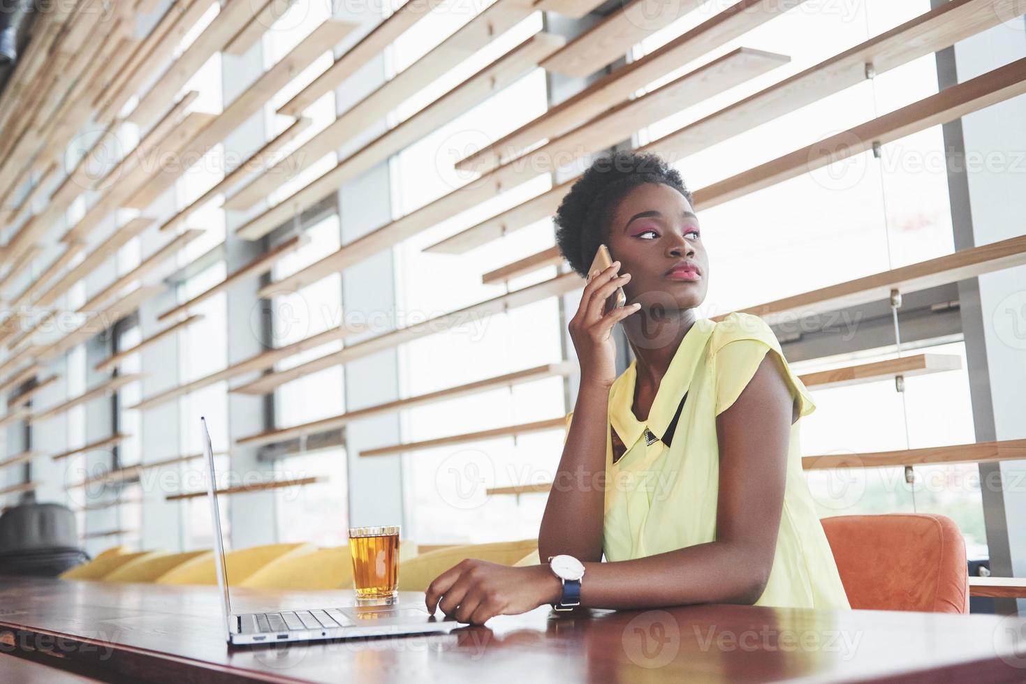 jeune belle femme d'affaires afro-américaine parlant au téléphone tout en travaillant dans un café photo