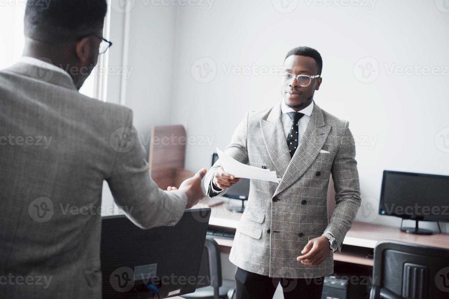 discuter d'un projet. deux hommes d'affaires noirs en tenue de soirée discutant de quelque chose tandis que l'un d'eux pointe un papier photo