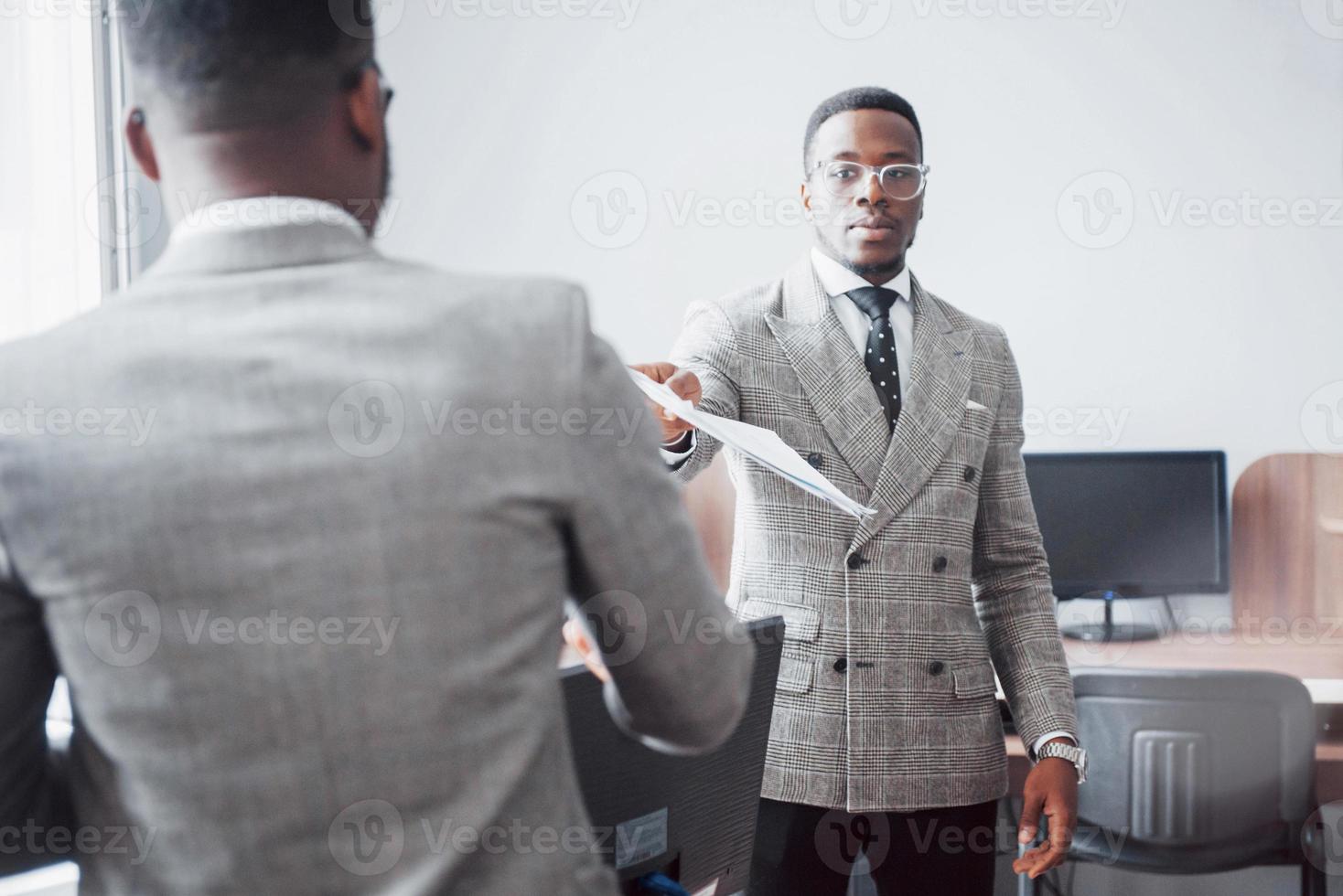 discuter d'un projet. deux hommes d'affaires noirs en tenue de soirée discutant de quelque chose tandis que l'un d'eux pointe un papier photo