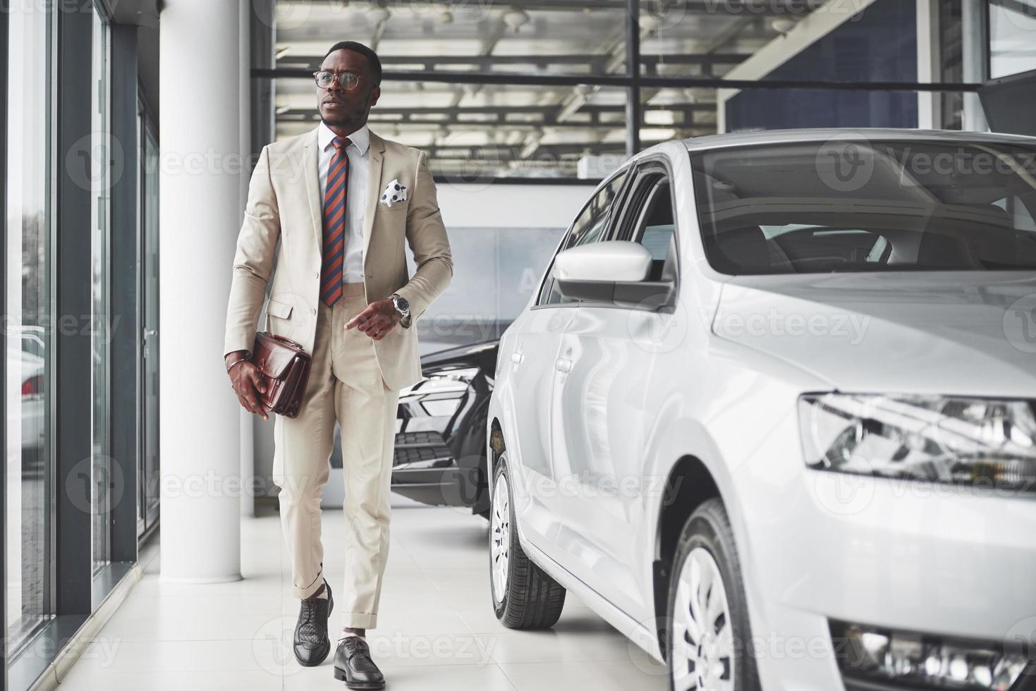 jeune homme d'affaires noir sur fond de salon automobile. concept de vente et de location de voiture photo