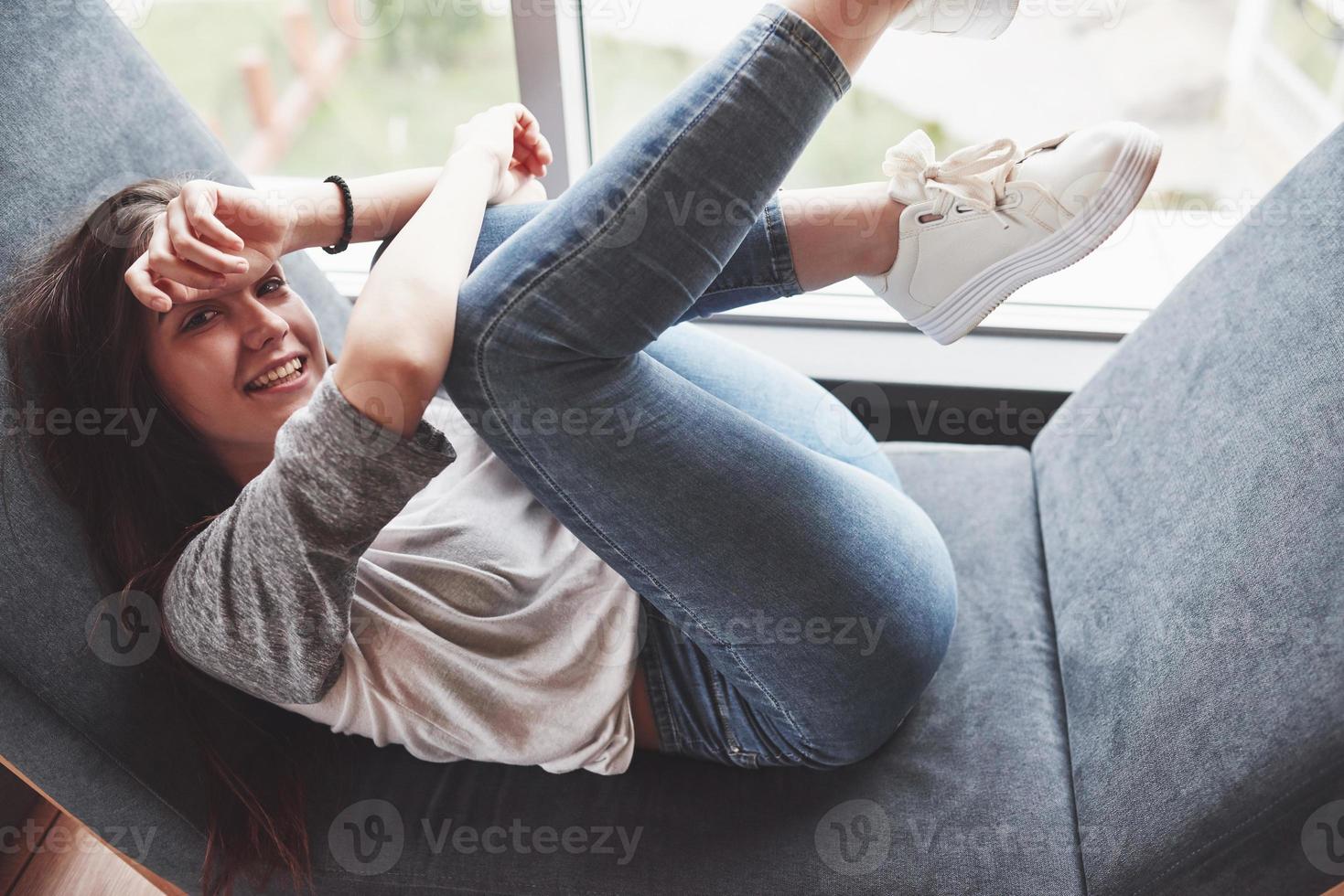 belle jeune fille passe son temps dans la zone de loisirs. elle s'assoit et s'amuse dans le fauteuil en forme d'hexagone avec des coussins près de la fenêtre photo