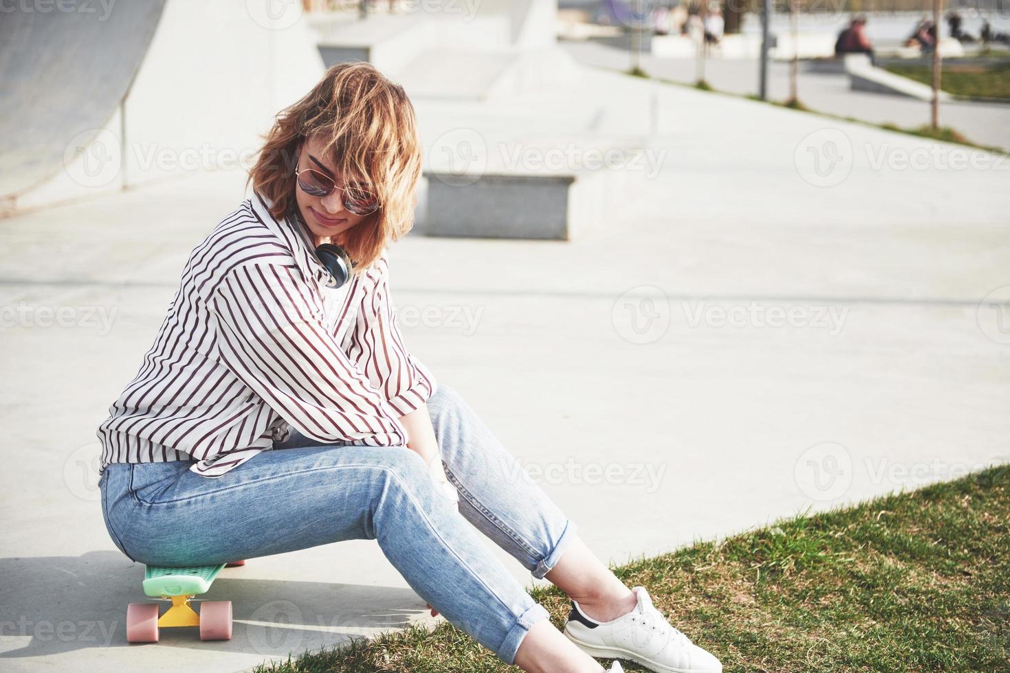 une belle jeune fille s'amuse dans le parc et fait du skateboard photo