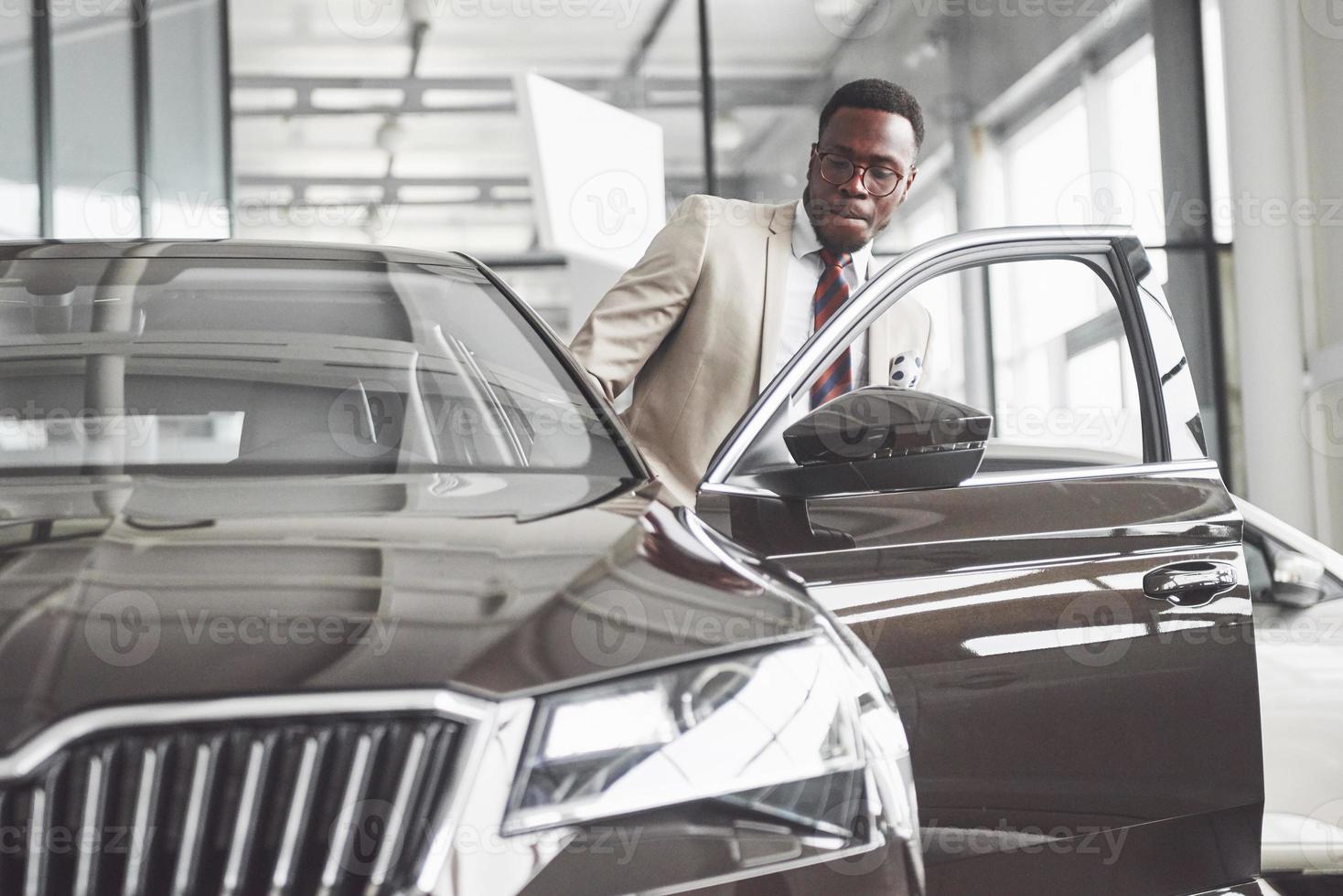 jeune homme d'affaires noir sur fond de salon automobile. concept de vente et de location de voiture photo