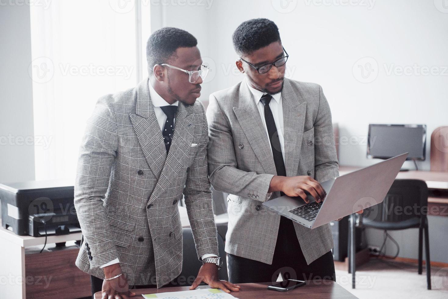 homme d'affaires moderne au travail. deux hommes d'affaires confiants en tenue de soirée discutent de quelque chose et regardent le moniteur d'ordinateur portable photo