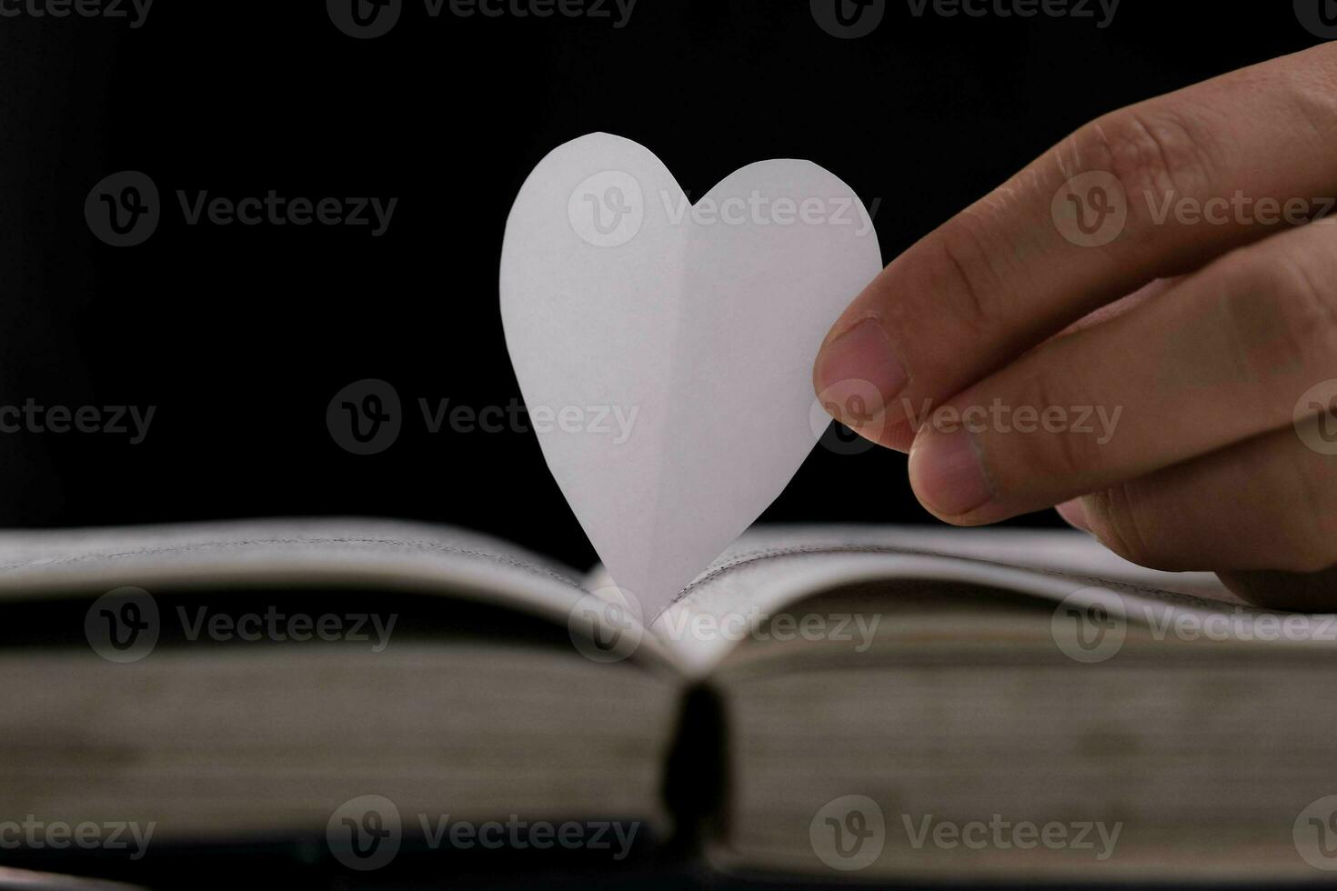 livre avec ouvert pages et cœur en forme de papier. femme main en portant cœur en forme de papier plus de ouvert livre sur tableau. l'amour de en train de lire concept photo