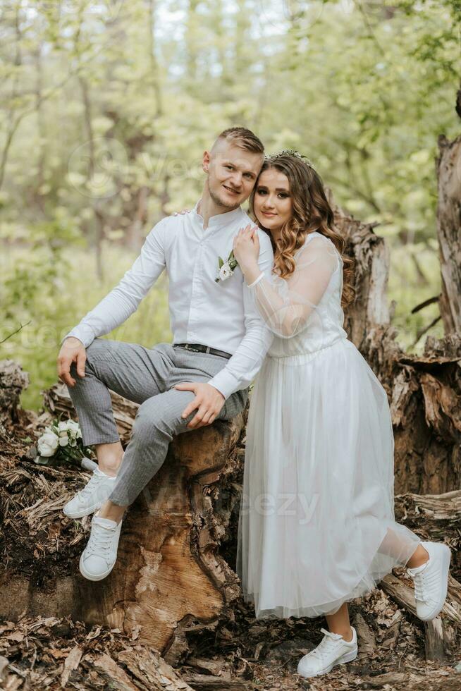 doux embrasse de le la mariée et jeune marié dans le forêt. le jeune marié est habillé dans une blanc chemise et gris pantalon, le la mariée est dans une lumière blanc robe photo