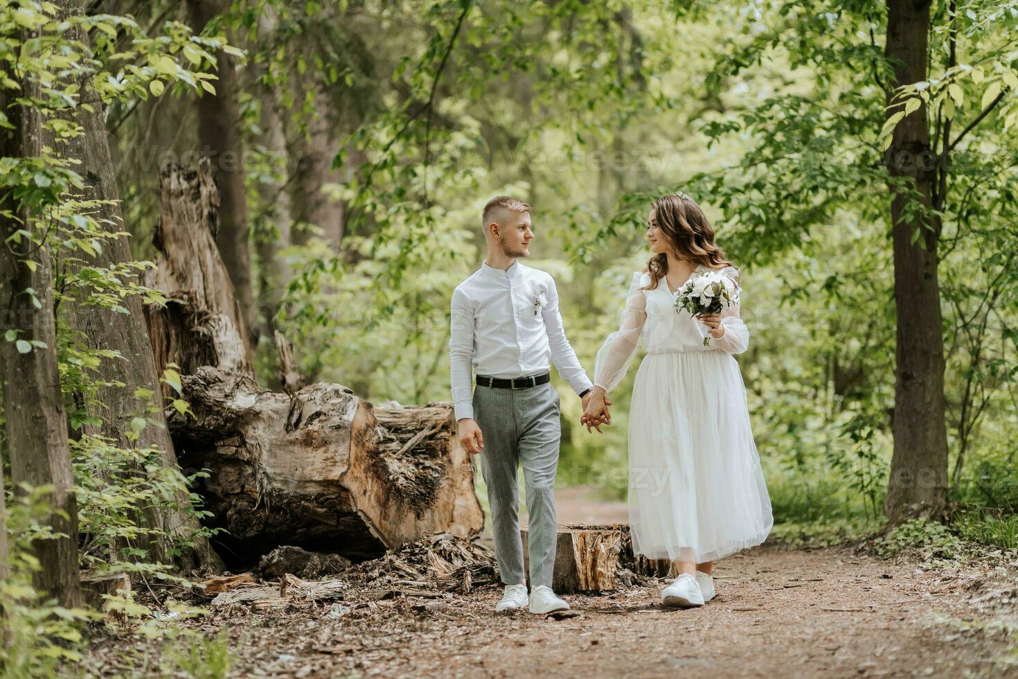 mariage marcher dans le forêt. le jeune marié détient le main de le la mariée et elles ou ils marcher dans de face de grand des arbres à la recherche à chaque autre photo